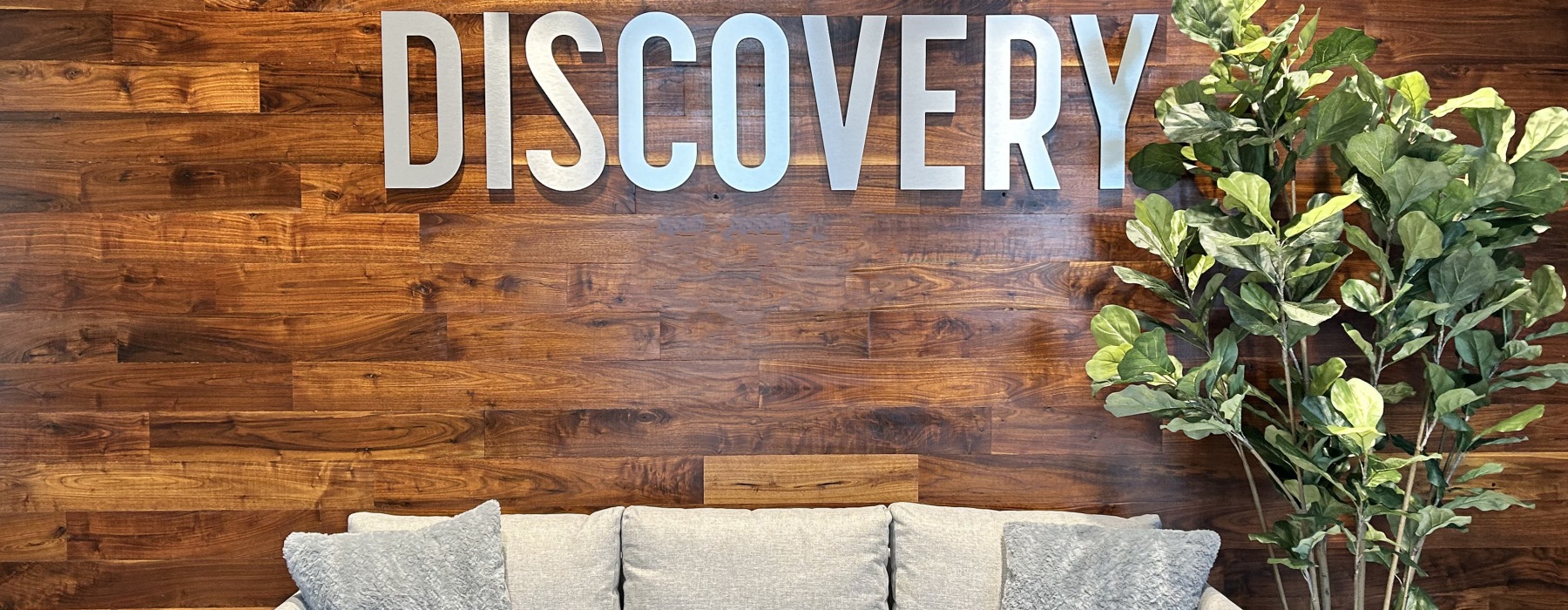 a couch in front of a wood wall with a sign on it next to a plant