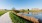a path next to a body of water with buildings in the background