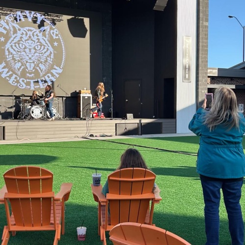 a person standing in a grassy area with chairs and tables in front of a stage